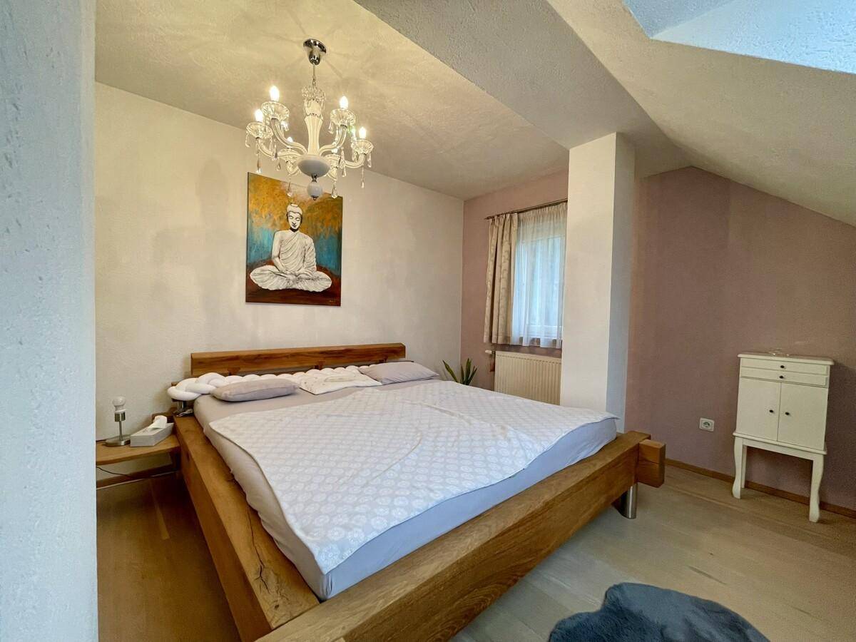 Ruhiges Schlafzimmer mit Holzbett, Kronleuchter und dekorativem Kunstwerk an der Wand.