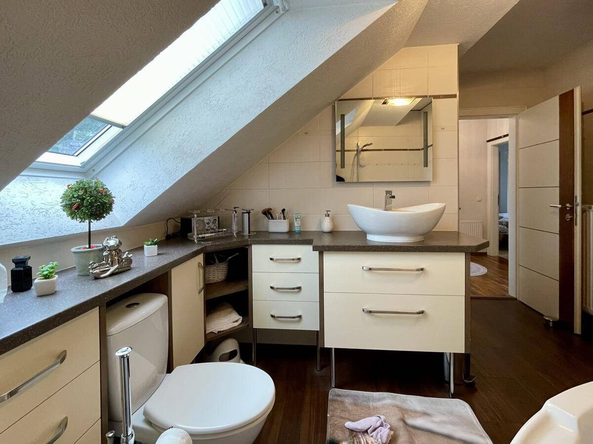 Modernes Badezimmer mit Waschtisch, Toilette, Spiegel und Dachfenster für natürliches Licht.