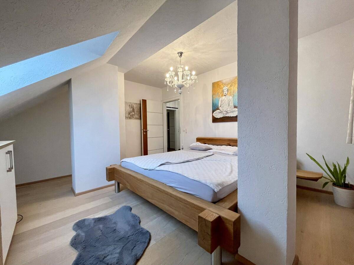 Helles Schlafzimmer mit Holzbett, Kronleuchter und Kunstwerk, das eine ruhige Atmosphäre schafft.