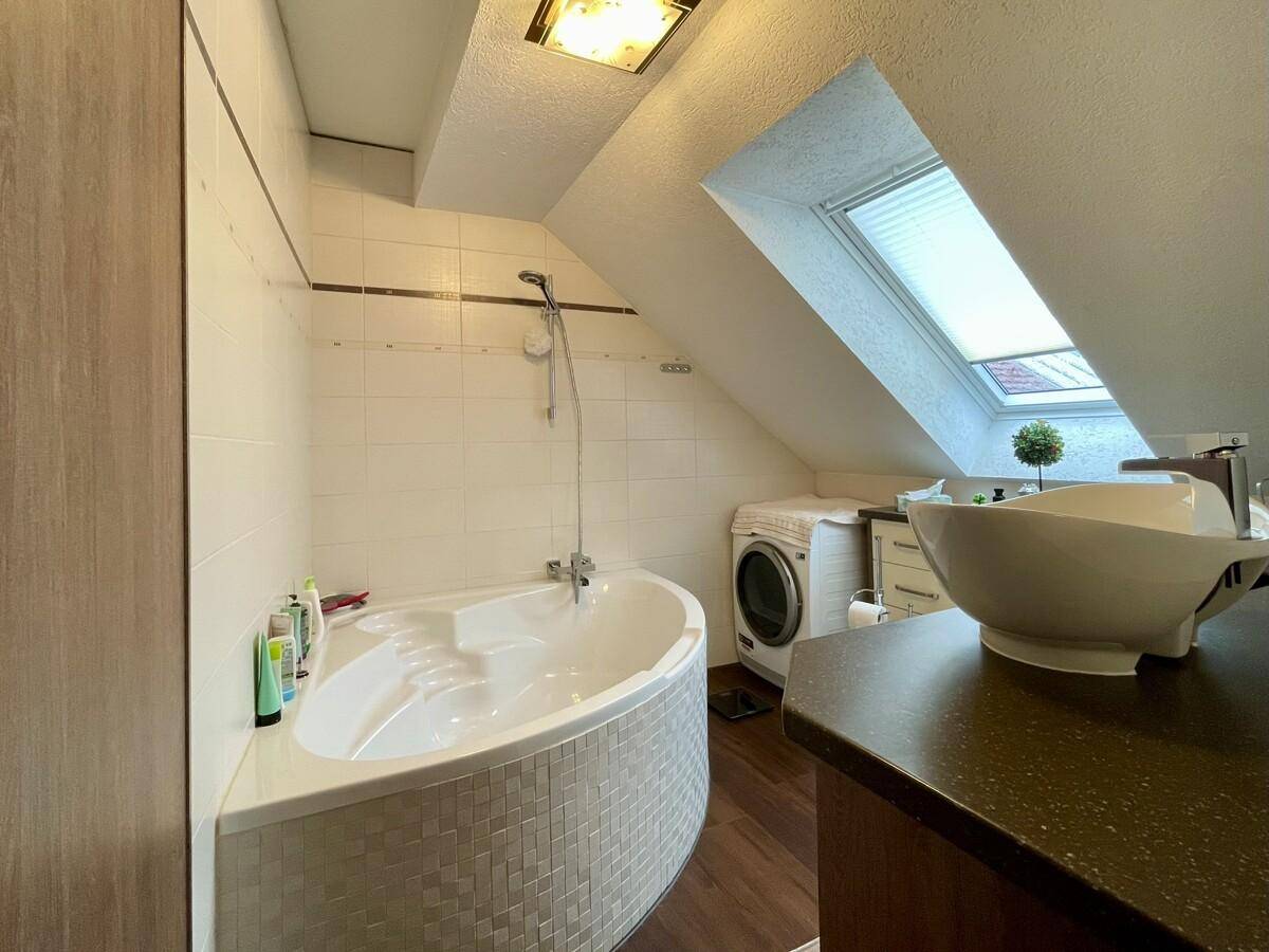 Geräumiges Badezimmer mit Eckbadewanne, Waschmaschine und Dachfenster.