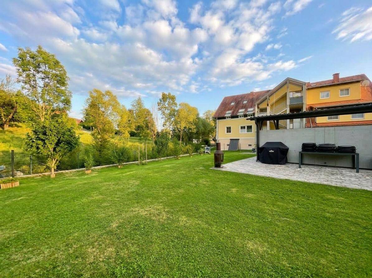 Großer, gepflegter Garten mit Rasenfläche, Bäumen und einem Grillbereich neben dem Haus.