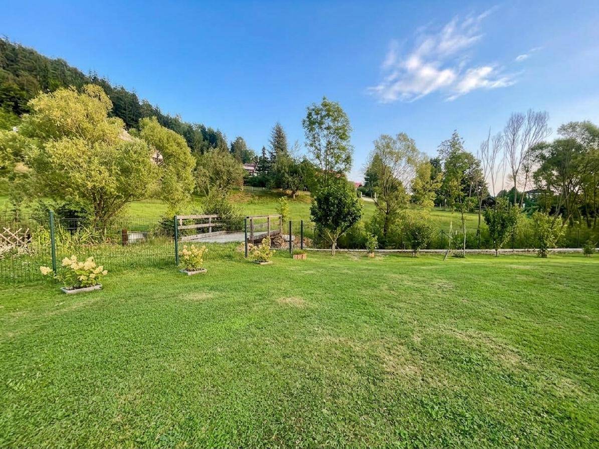 Weitläufiger grüner Garten mit Rasenfläche und Bäumen, umgeben von einer natürlichen Hügellandschaft.