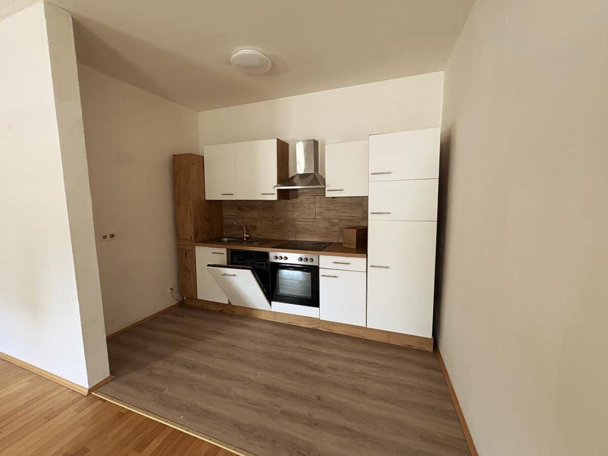 Moderne Einbauküche mit weißen Fronten, integrierten Geräten und Laminatboden in einem leeren Raum.