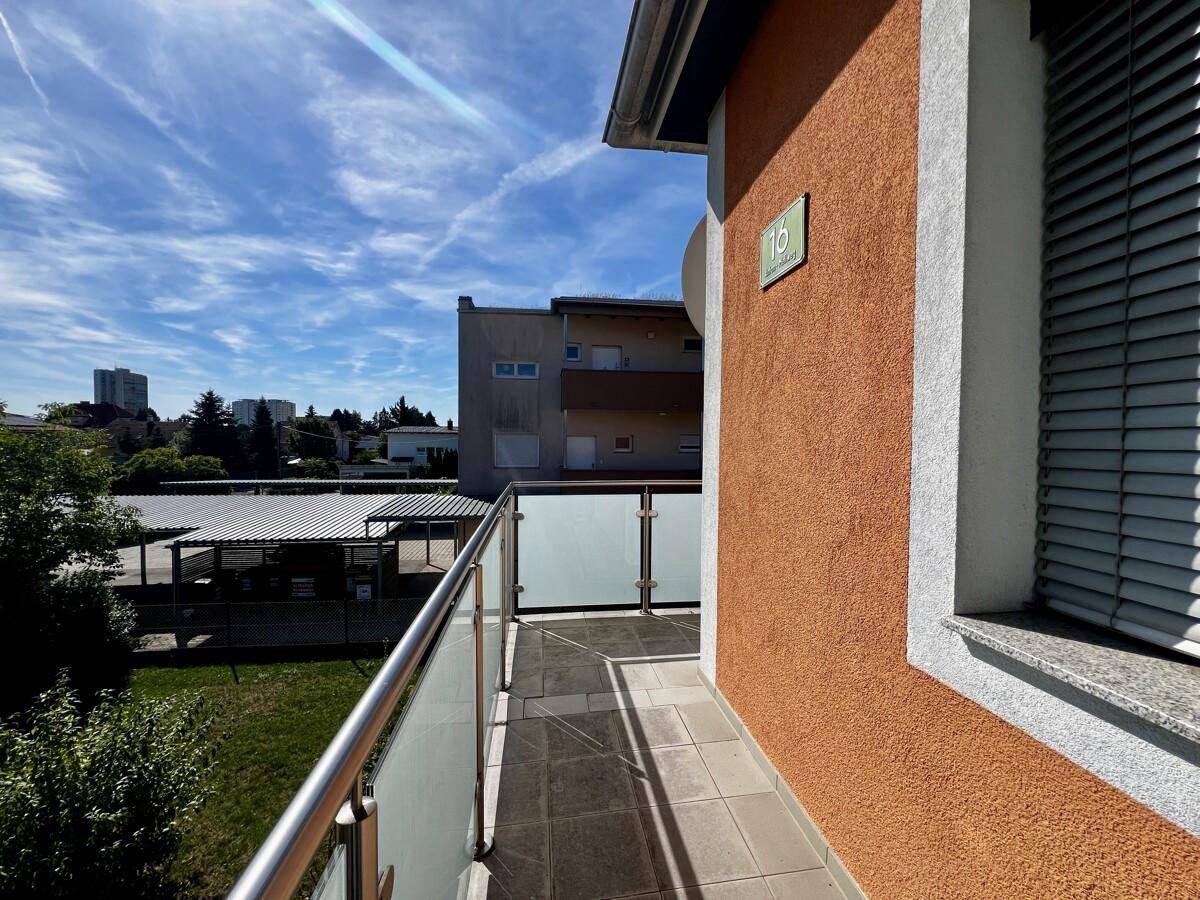 Heller Balkon mit Glasgeländer und Blick auf die umliegende Wohngegend und Grünflächen.