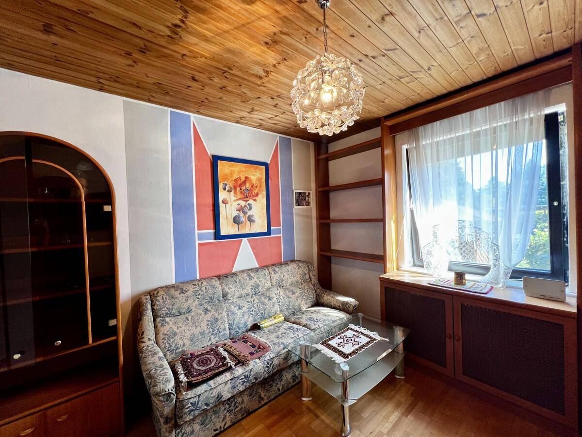 Wohnzimmer mit Sofa, Glas-Couchtisch, Holzdecke und dekorativ gestrichener Wand.