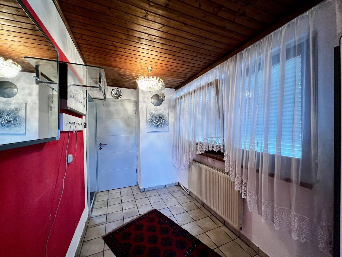 Eingangsbereich mit Fliesenboden, roter Akzentwand und einer Holzpaneeldecke.