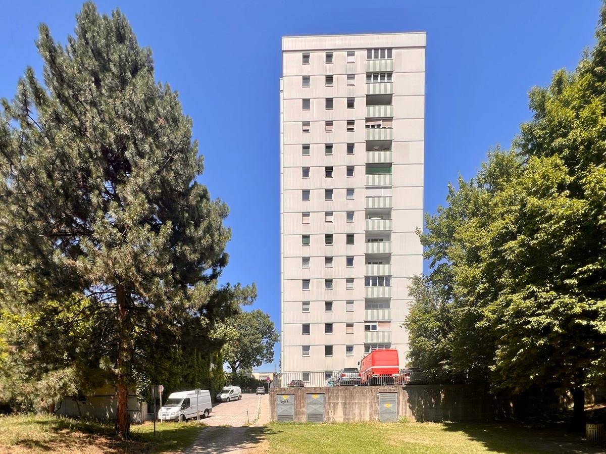 Frontansicht des hohen Wohnhauses mit zahlreichen Fenstern und Balkonen unter blauem Himmel.