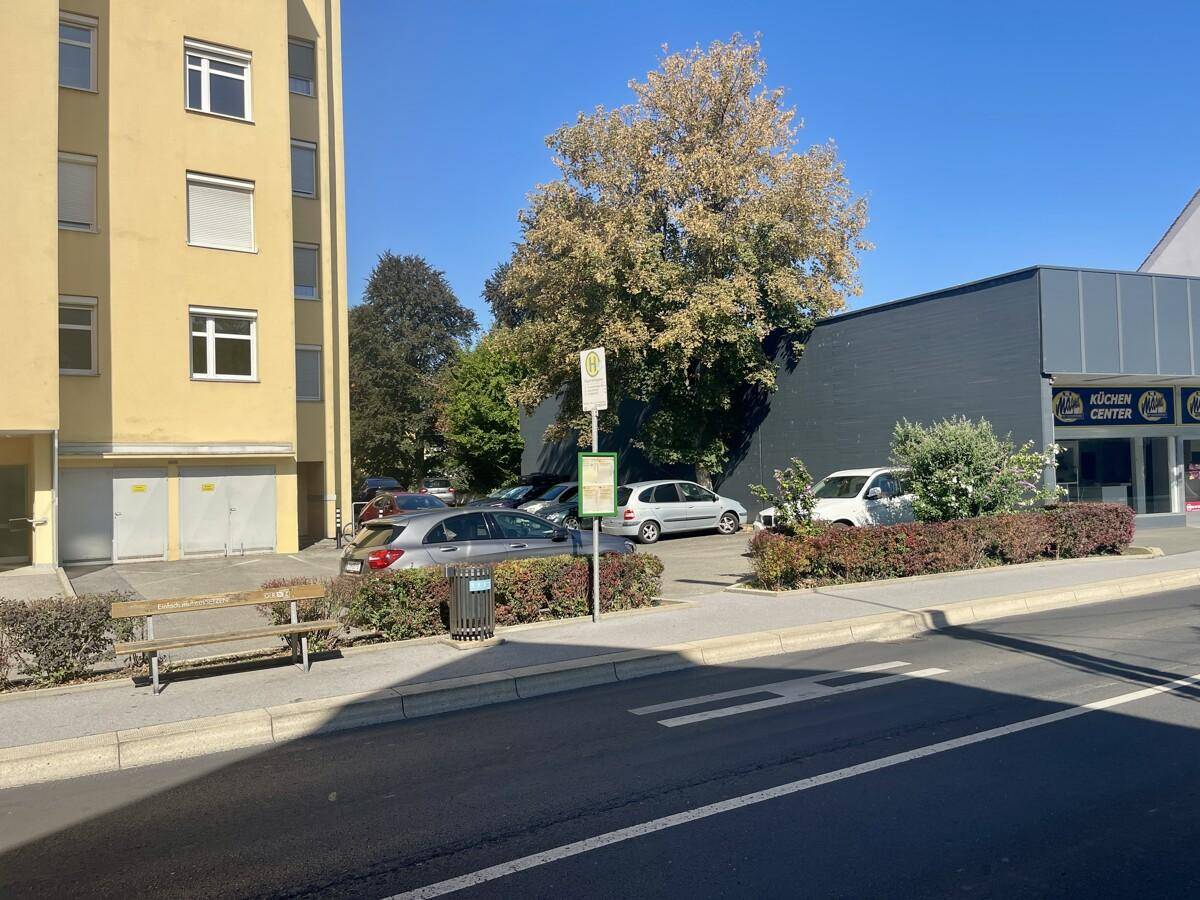 Straßenansicht neben dem Wohngebäude mit geparkten Autos und einem Küchenstudio im Hintergrund.