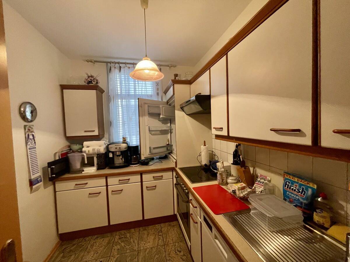 Funktionale Küche mit weißen Schränken, Holzdetails und Fliesenboden, ausgestattet mit Geräten.