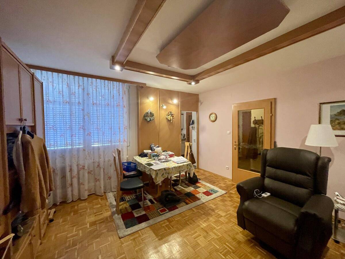 Wohnbereich mit Fenster, Vorhängen, kleinem Esstisch und bequemen Sitzgelegenheiten.