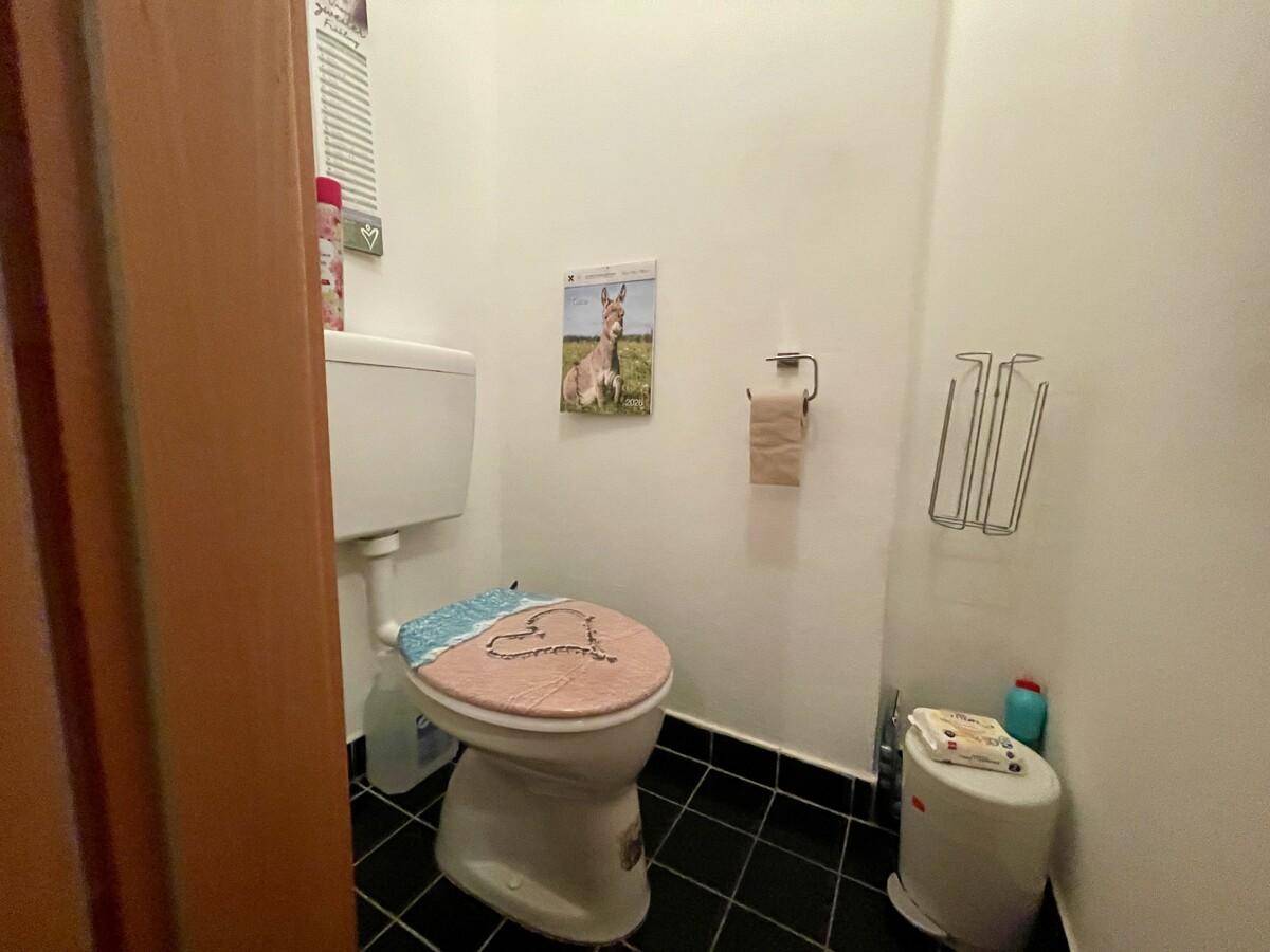 Kleines separates WC mit Toilette und dunklem Fliesenboden, funktional eingerichtet.