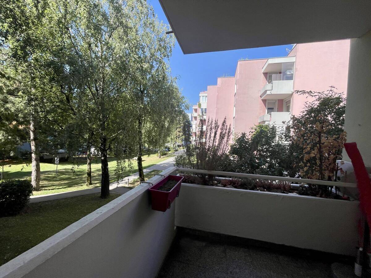 Balkon mit Blick ins Grüne und auf weitere Wohngebäude unter blauem Himmel.