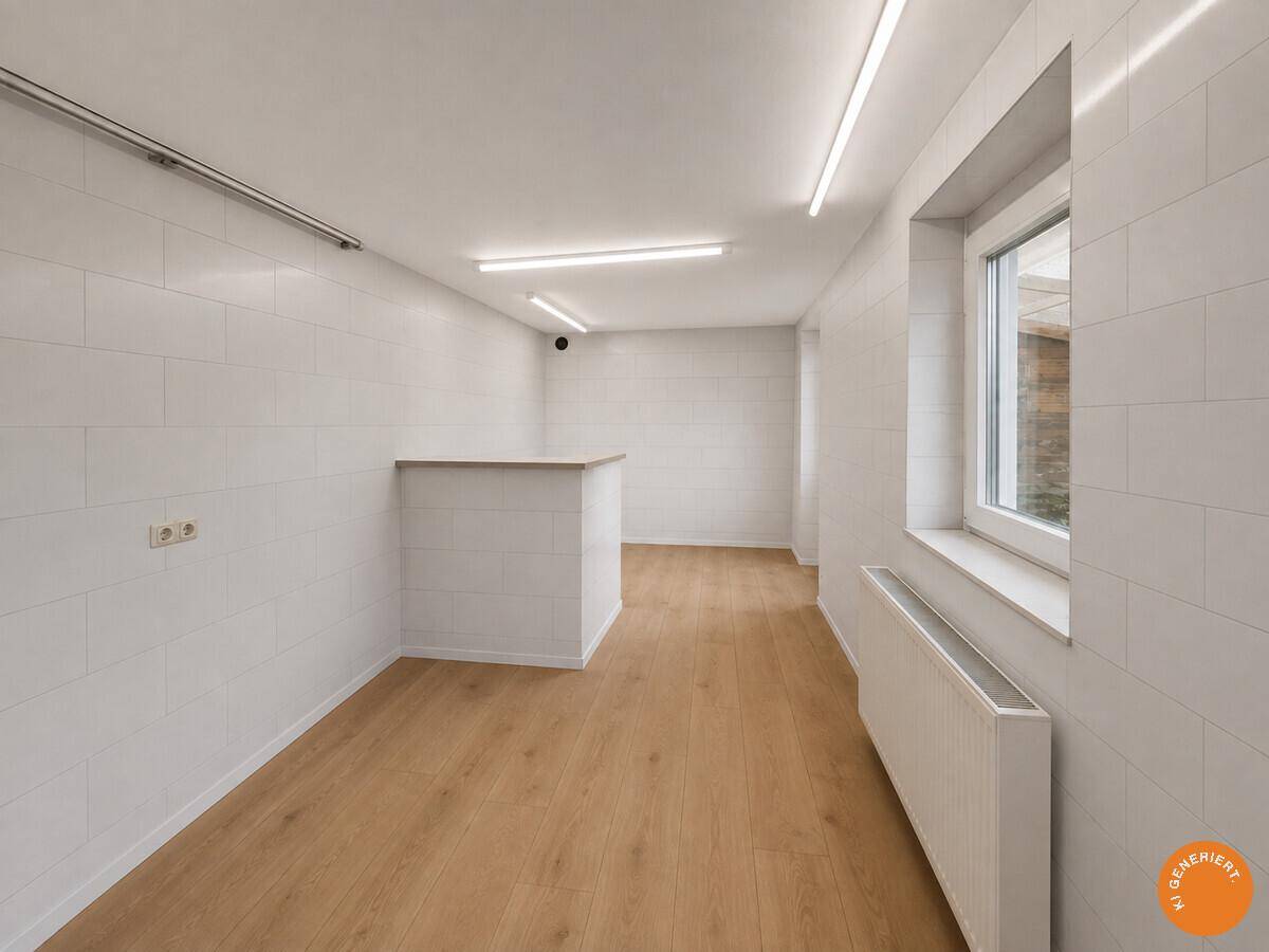 Leerer Raum mit hellen Wänden, Laminatboden und einem großen Fenster, das viel Licht hereinlässt.