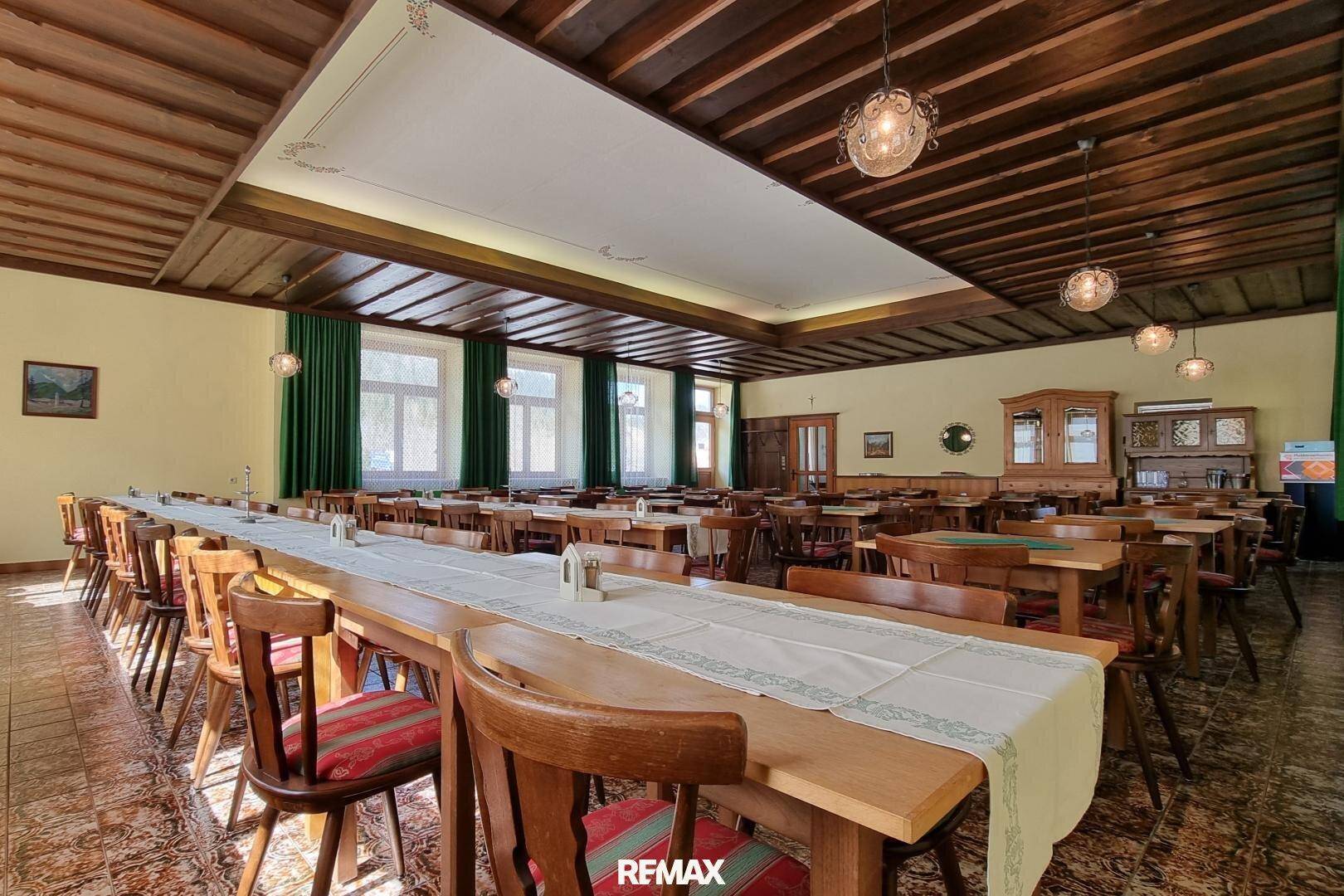 Großer Speisesaal mit Holzbalkendecke, langen Tischen und vielen Fenstern, ideal für Veranstaltungen.