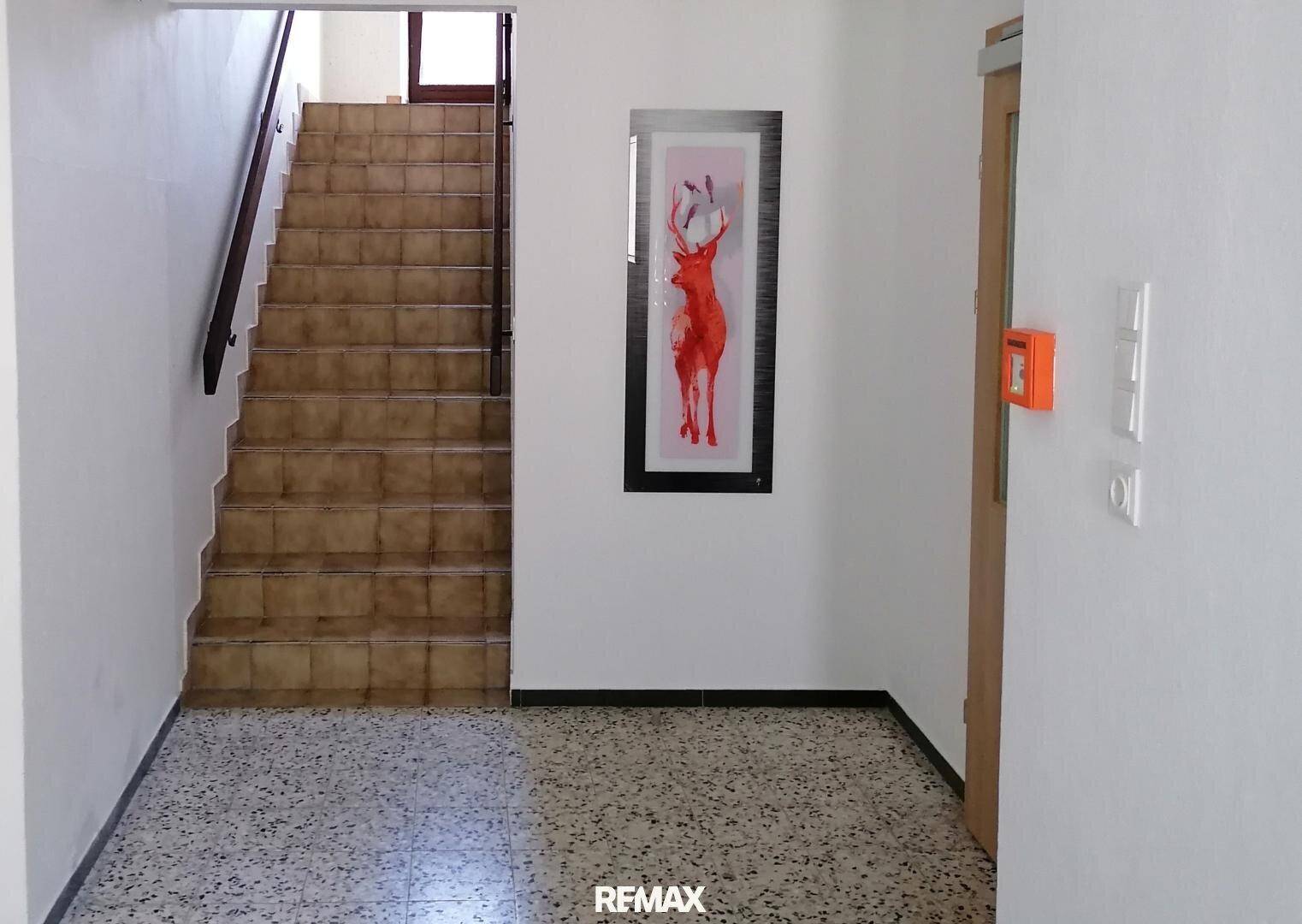 Heller Flur mit Terrazzoboden, einer Fliesentreppe und einem Hirschbild an der Wand.