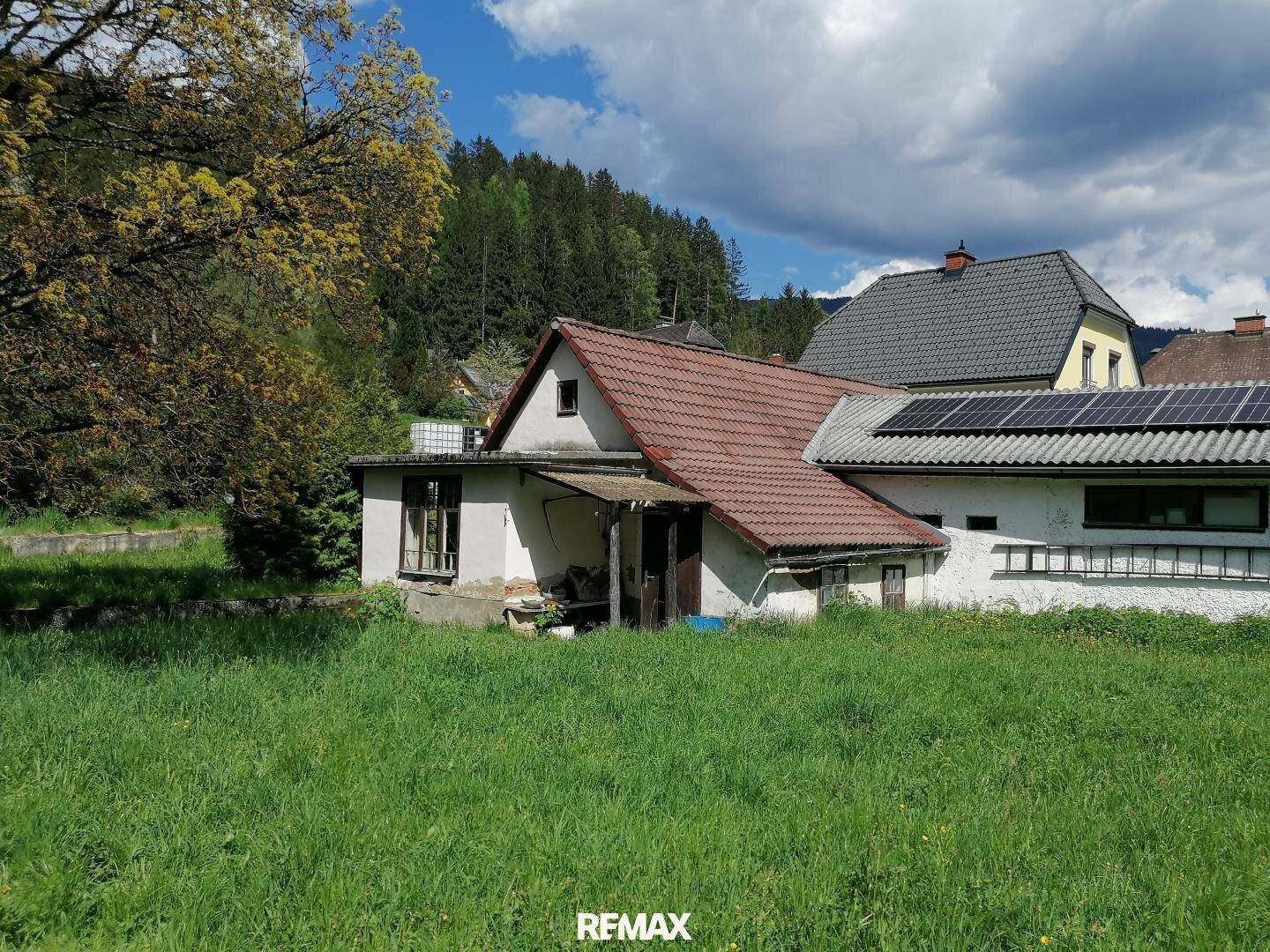 Haus mit rotem Ziegeldach und Solaranlage auf dem Nebengebäude, umgeben von Wiesen.