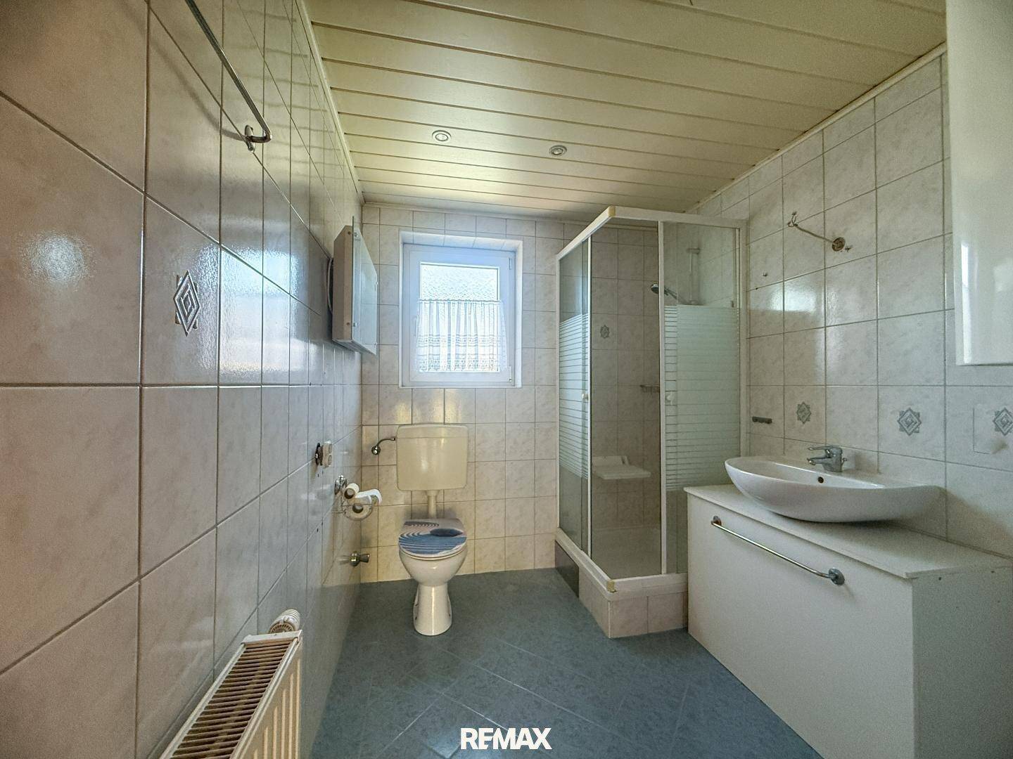 Gefliestes Badezimmer mit Dusche, WC und Waschbecken, ausgestattet mit einem Fenster.