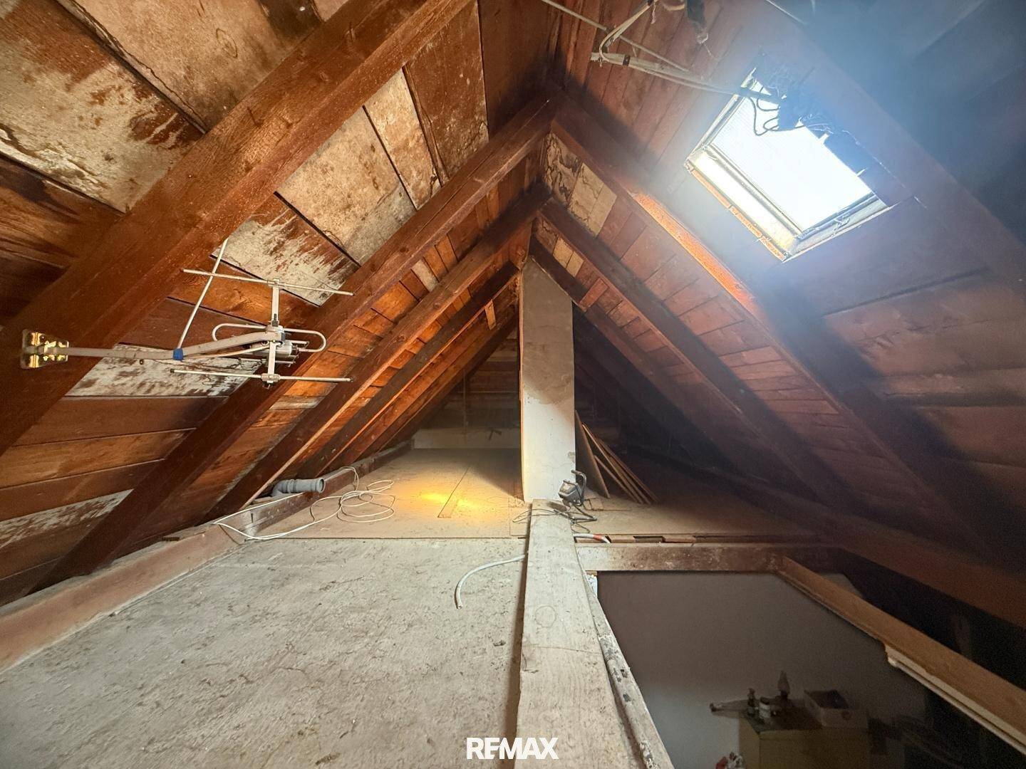Geräumiger Dachboden mit sichtbaren Holzbalken und einem Dachfenster für Tageslicht.