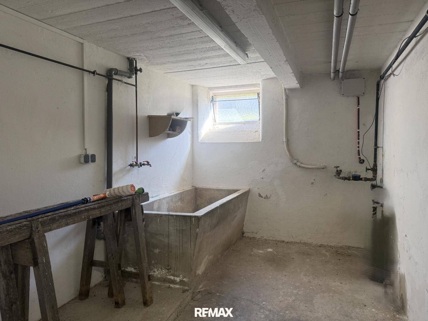 Waschküche im Keller mit großem Waschbecken und Fenster, ideal für Hausarbeiten.
