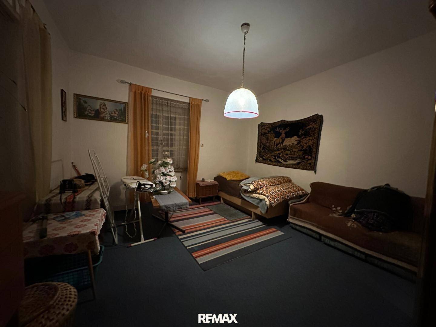 Einfaches Schlafzimmer mit Teppichboden, einem Bett und einem Sofa, spärlich beleuchtet.
