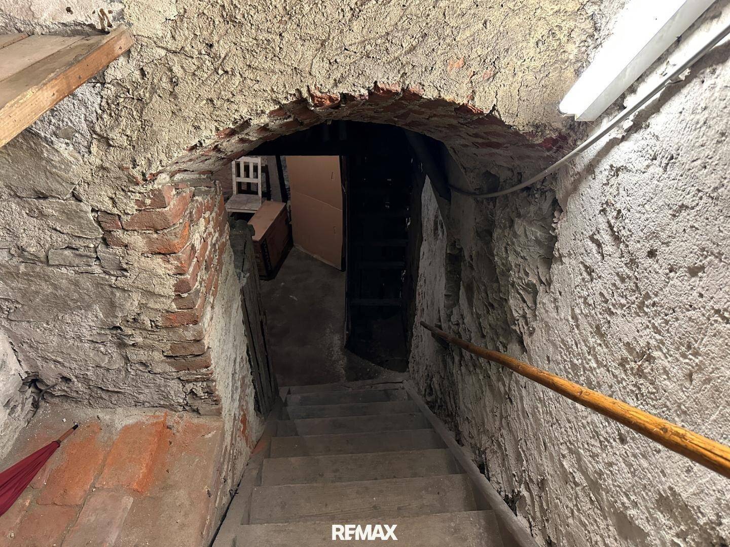 Historischer Kellerraum mit Steintreppe und unverputzten Ziegelwänden, ideal für Lagerung.
