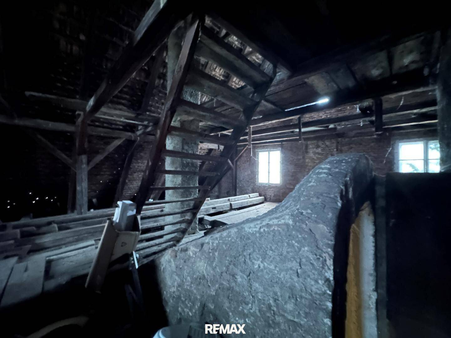 Geräumiger Dachboden mit sichtbaren Holzbalken und einer Holztreppe, die zu weiteren Ebenen führt.