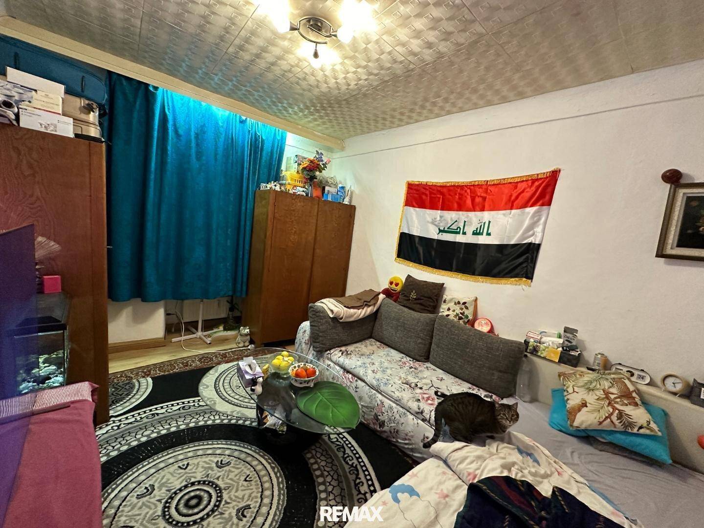 Wohnzimmer mit Sofa, Teppich und farbigen Vorhängen, dekoriert mit einer Flagge.