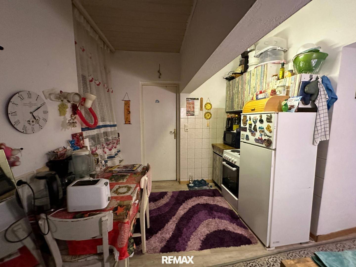 Gemütliche Wohnküche mit Esstisch, Kühlschrank und einfachen Küchenzeile.