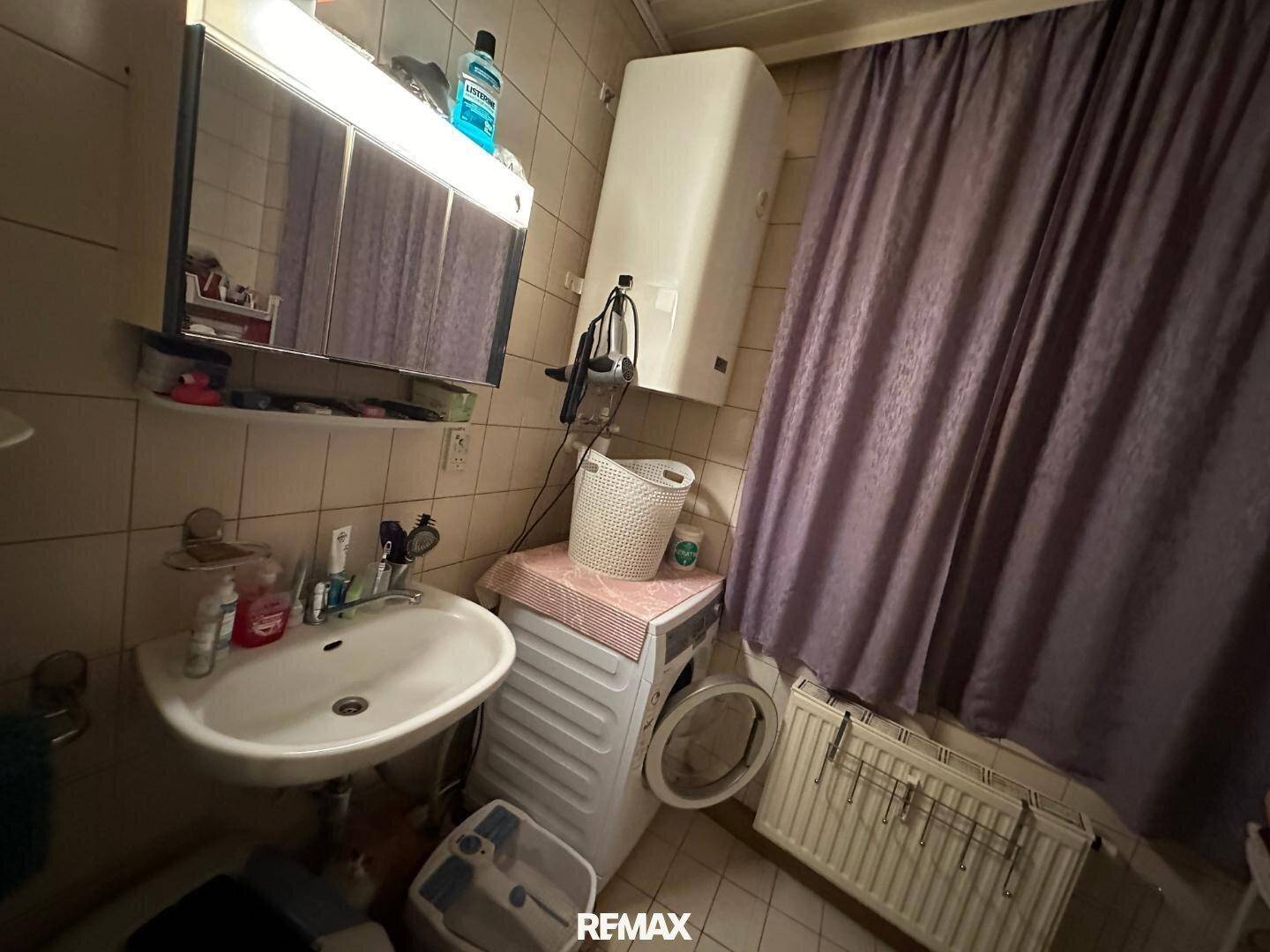 Kleines Badezimmer mit Waschbecken, Toilette, Dusche und einer Waschmaschine.