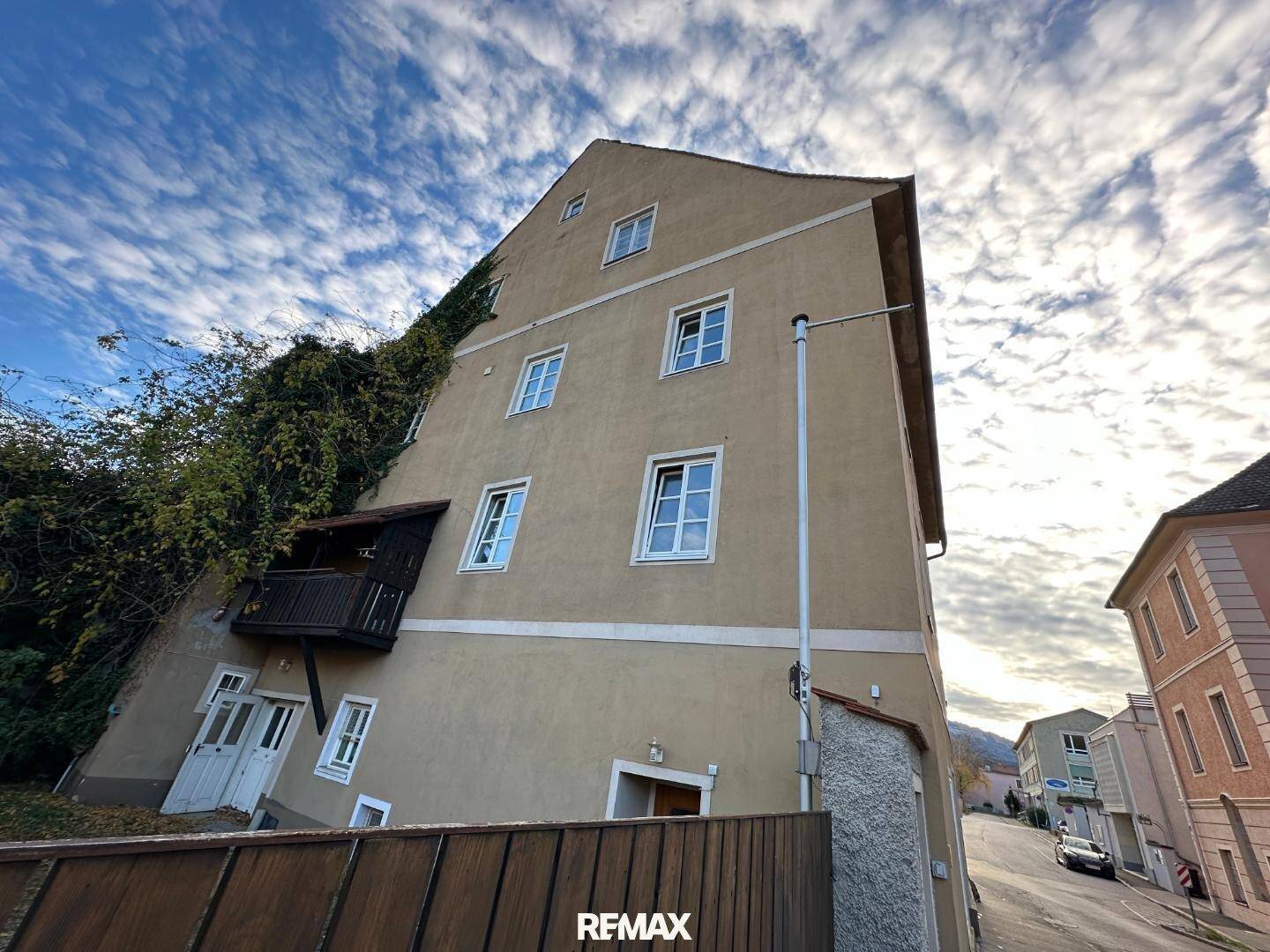 Seitenansicht eines älteren Gebäudes mit Bewuchs an der Wand und einem kleinen Holzbalkon.
