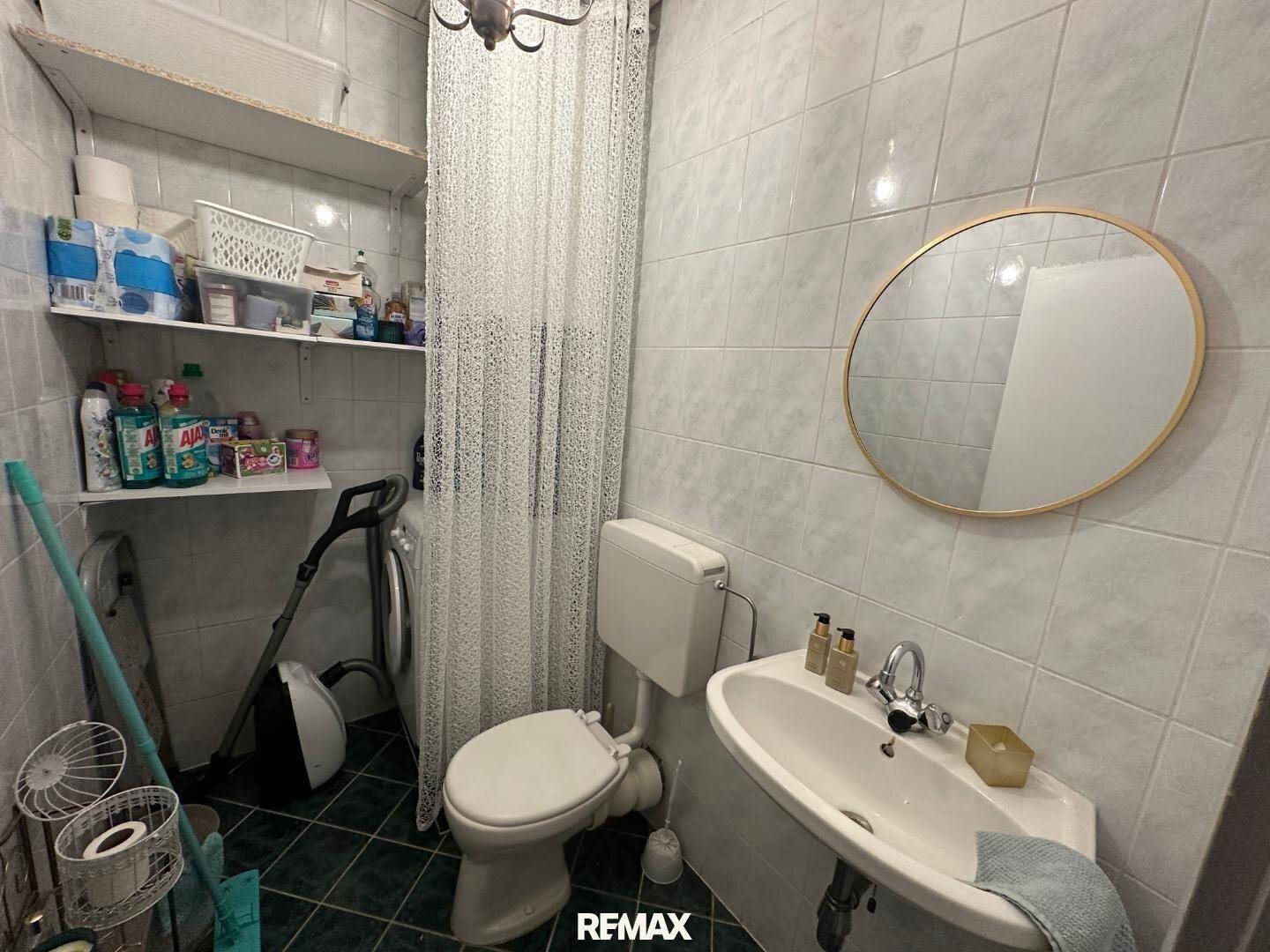 Kleines Badezimmer mit Toilette, Waschbecken und praktischen Regalen für Haushaltsartikel.
