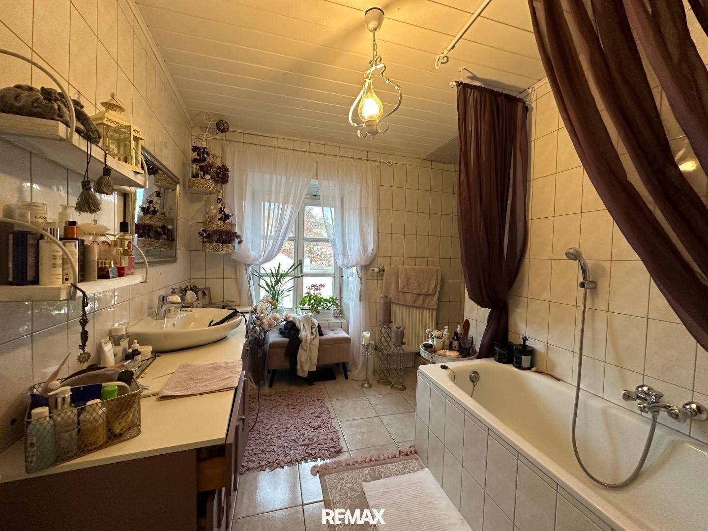 Geräumiges Badezimmer mit Badewanne, Waschbecken und Fenster, dekoriert mit Vorhängen.