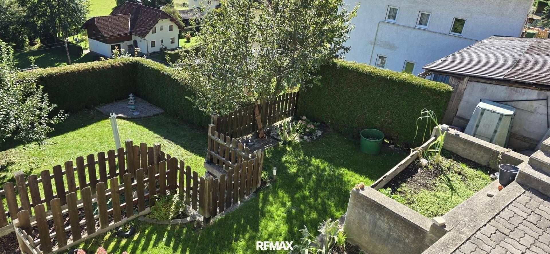 Gepflegter Gartenbereich mit Rasenfläche, Hecken und erhöhten Pflanzbeeten.
