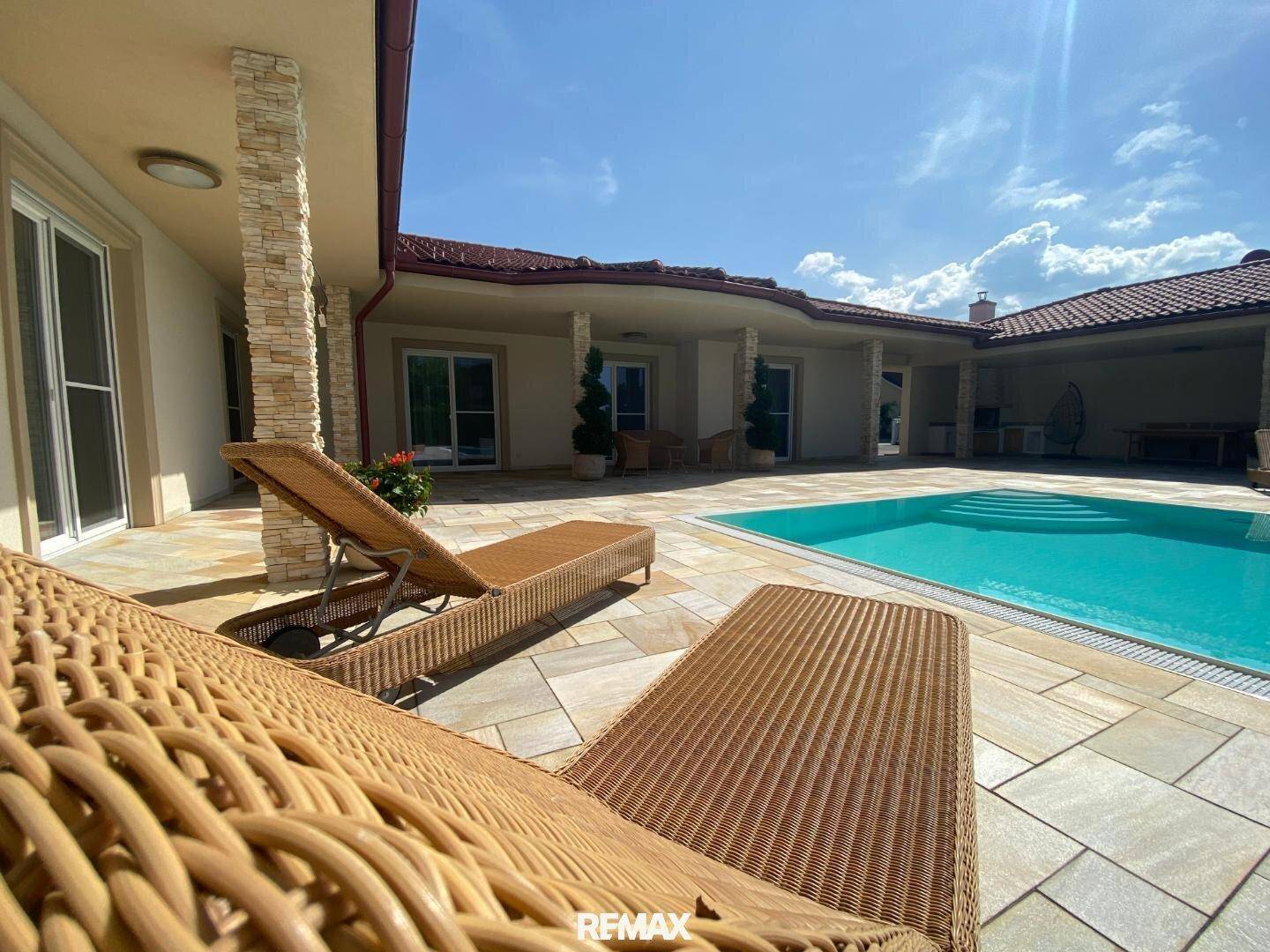 Entspannende Liegestühle am Pool auf der großzügigen Terrasse unter blauem Himmel.
