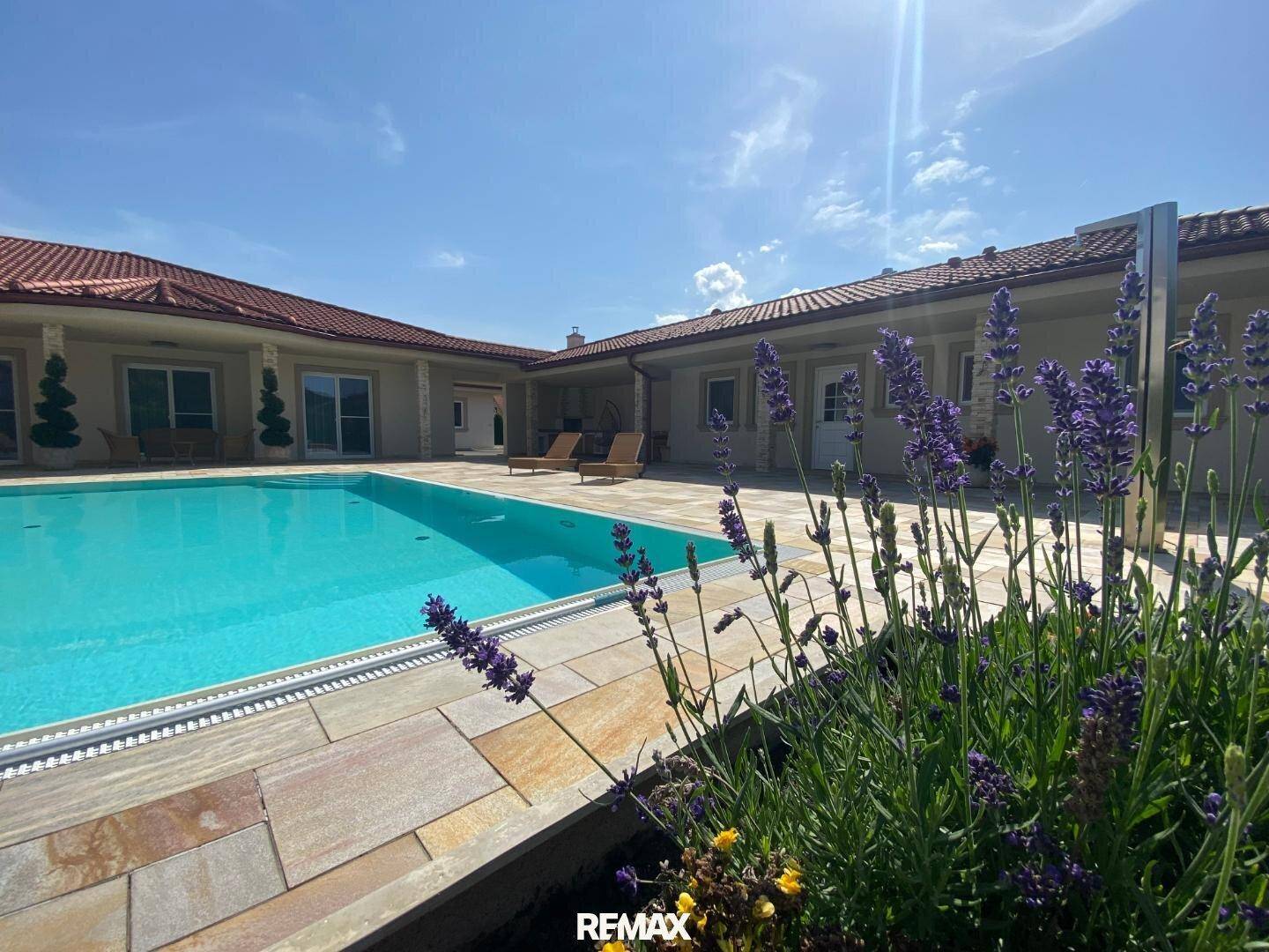 Großer Außenpool mit gefliester Terrasse und blühendem Lavendel unter strahlend blauem Himmel.