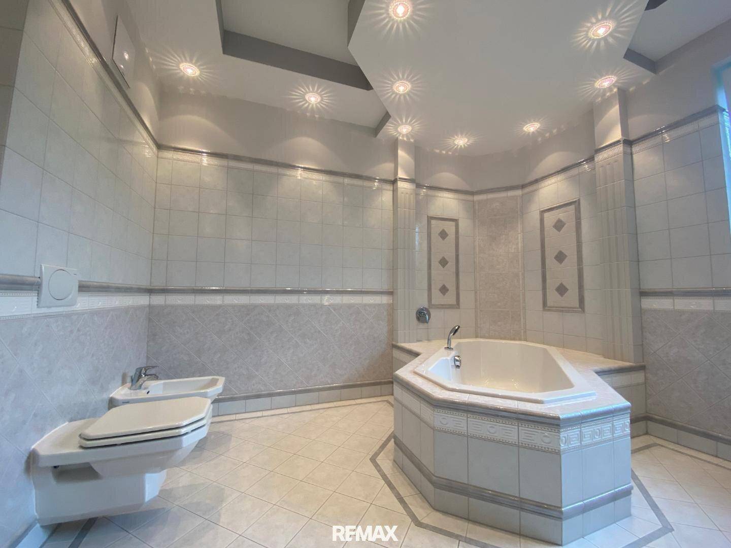 Geräumiges Badezimmer mit Eckbadewanne, Bidet und Wand-WC, komplett gefliest und mit Einbaustrahlern.