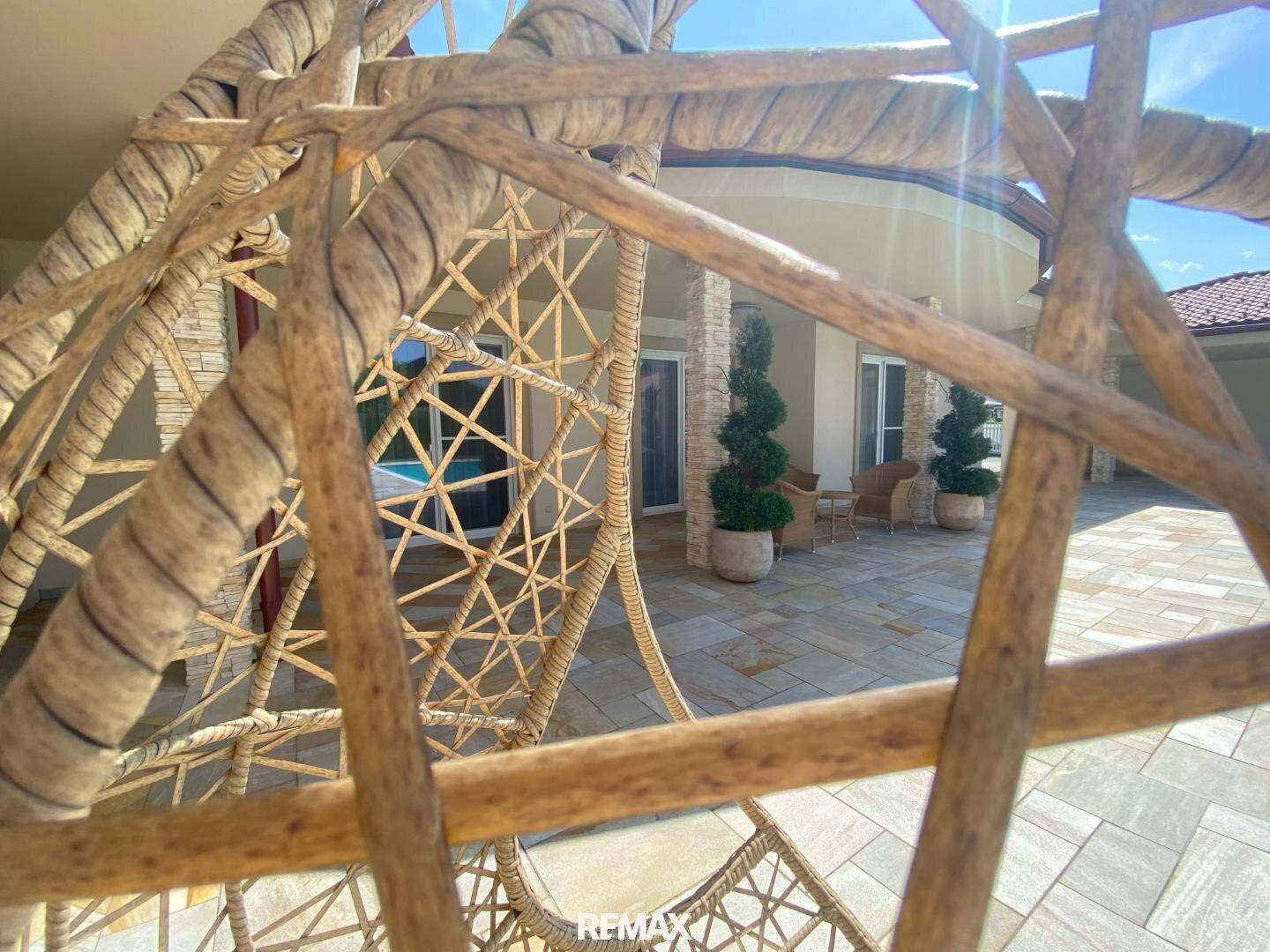 Detailaufnahme eines Hängesessels mit Blick auf den sonnigen Poolbereich und die Terrasse.