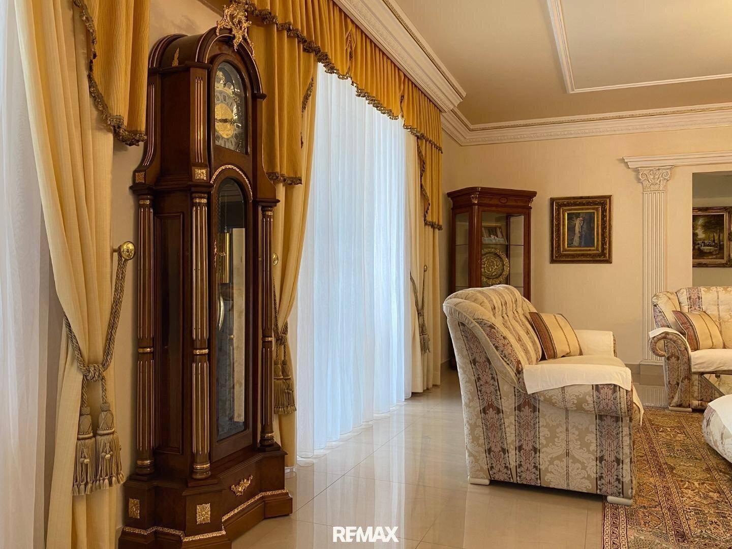 Detailansicht einer antiken Standuhr und eleganter Vorhänge im luxuriösen Wohnzimmer.
