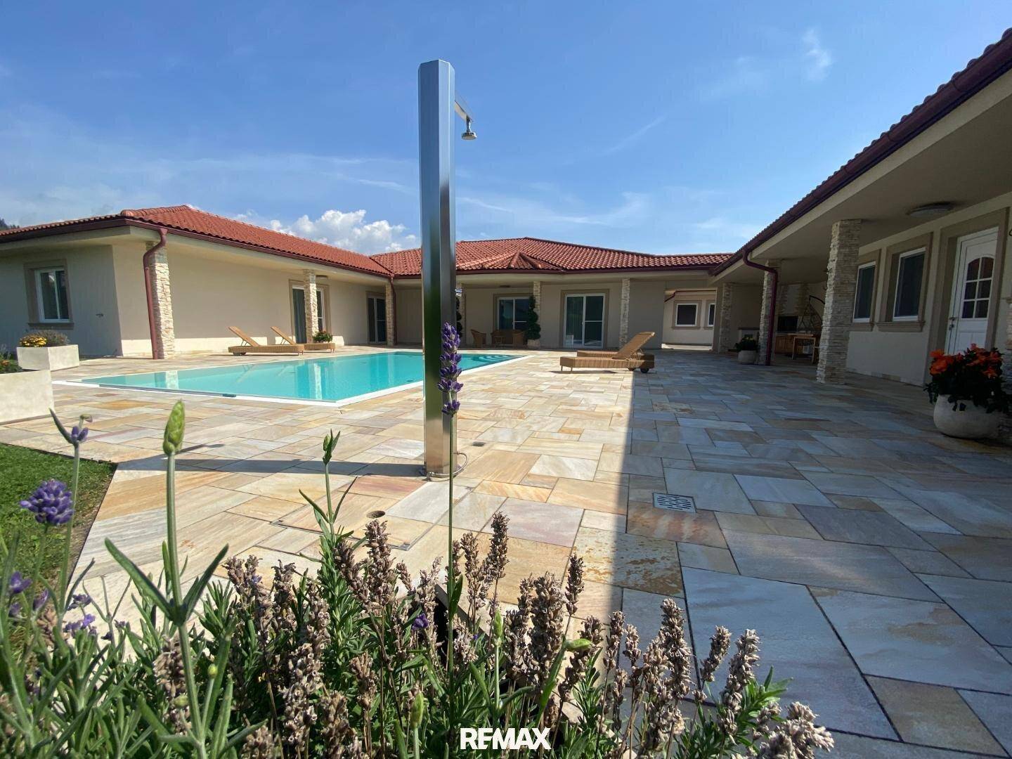 Weitläufige Poolanlage mit moderner Außendusche und sonniger Terrasse, umgeben von blühendem Lavendel.