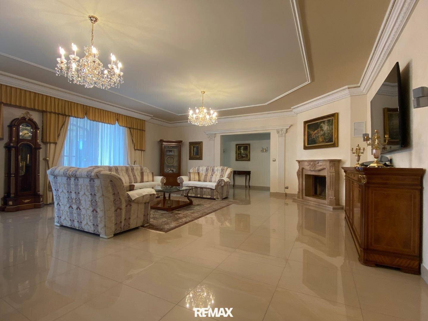 Großzügiges Wohnzimmer mit eleganten Kronleuchtern, klassischen Möbeln und glänzenden Fliesen.