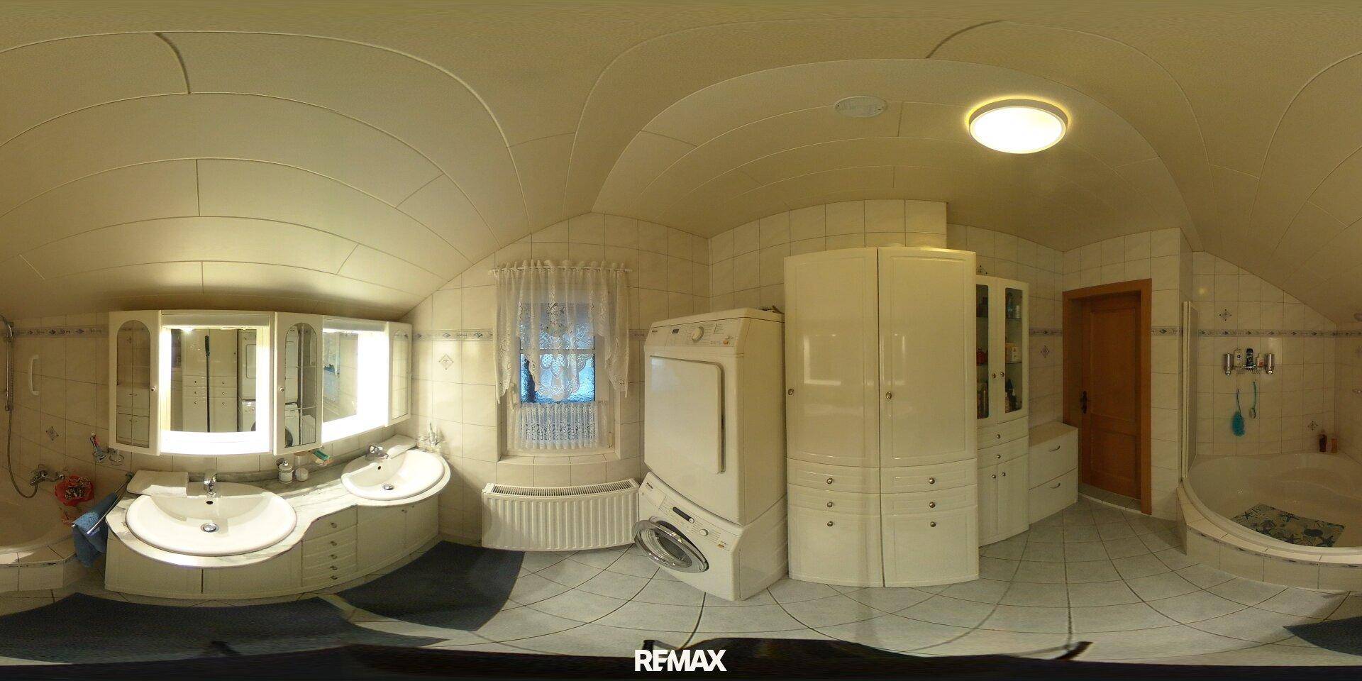 Helles Badezimmer mit Doppelwaschbecken, Badewanne, Waschmaschine und Trockner unter Dachschräge.