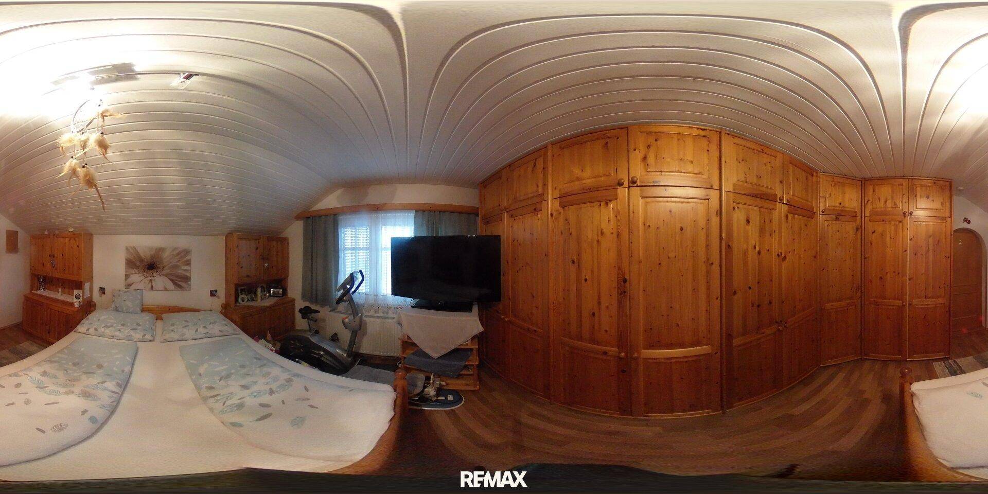 Gemütliches Schlafzimmer unter dem Dach mit großen Holzschränken, Doppelbett und Fernseher.