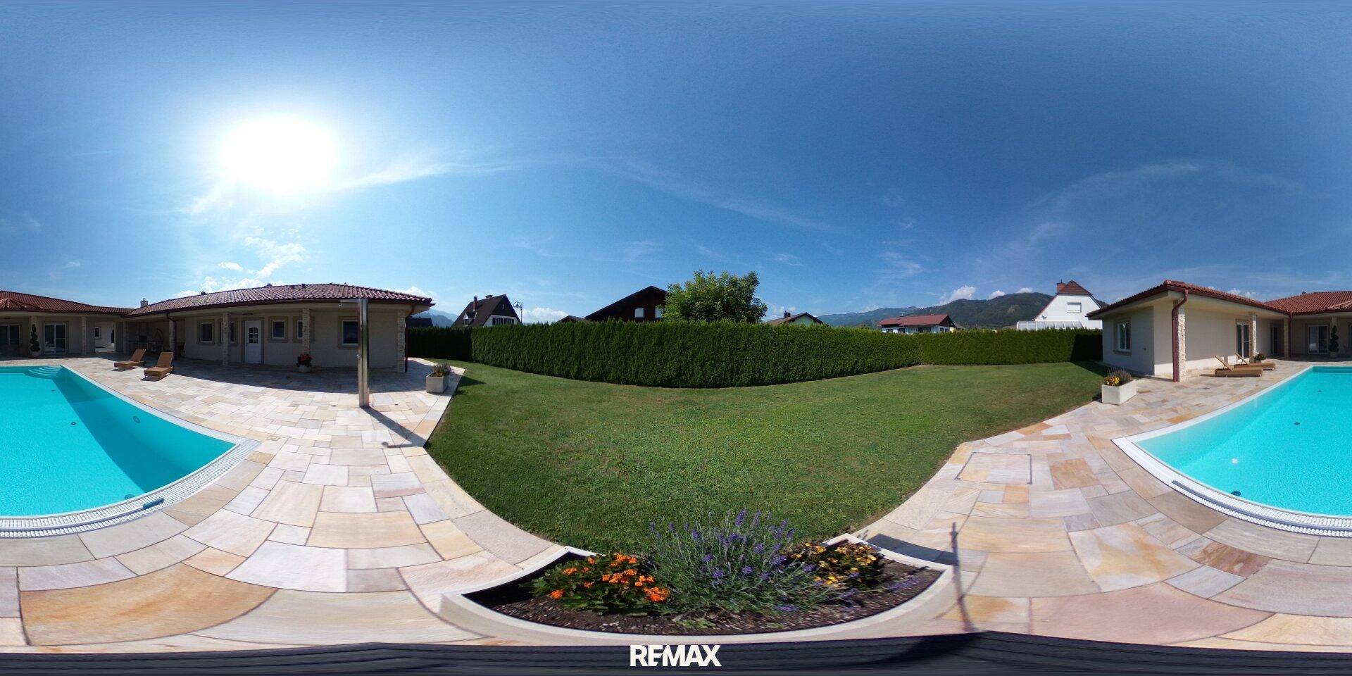 Panoramablick auf den weitläufigen Garten mit Rasenfläche, Pool und gepflegter Hecke.