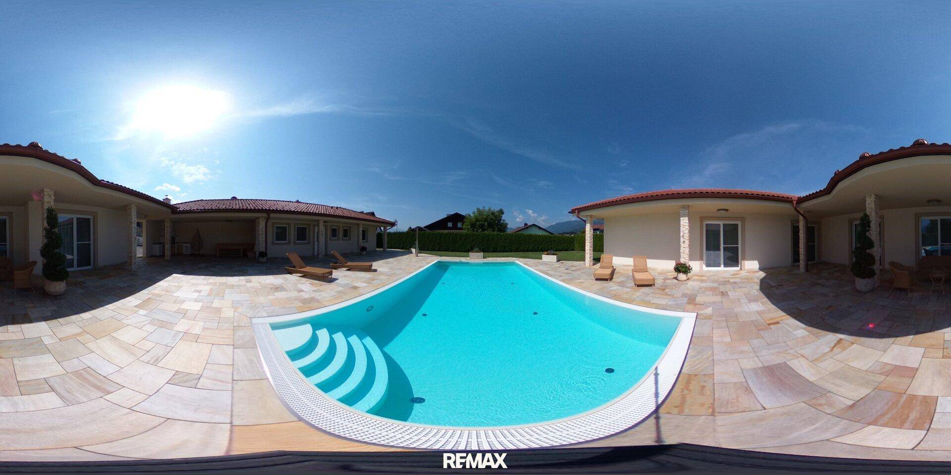 Panoramaansicht der weitläufigen Poolanlage mit geschwungenem Becken und umliegender Sonnenterrasse.