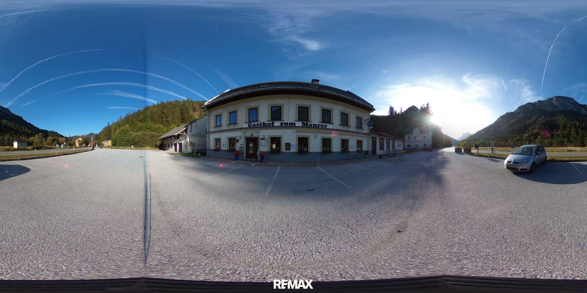 Eine 360-Grad-Außenansicht des Gasthofs mit großem Parkplatz unter blauem Himmel.