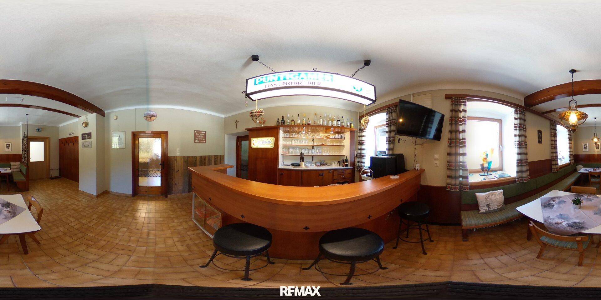 Panoramablick auf eine traditionelle Bar mit Holztheke, Barhockern und Regalen voller Getränke.