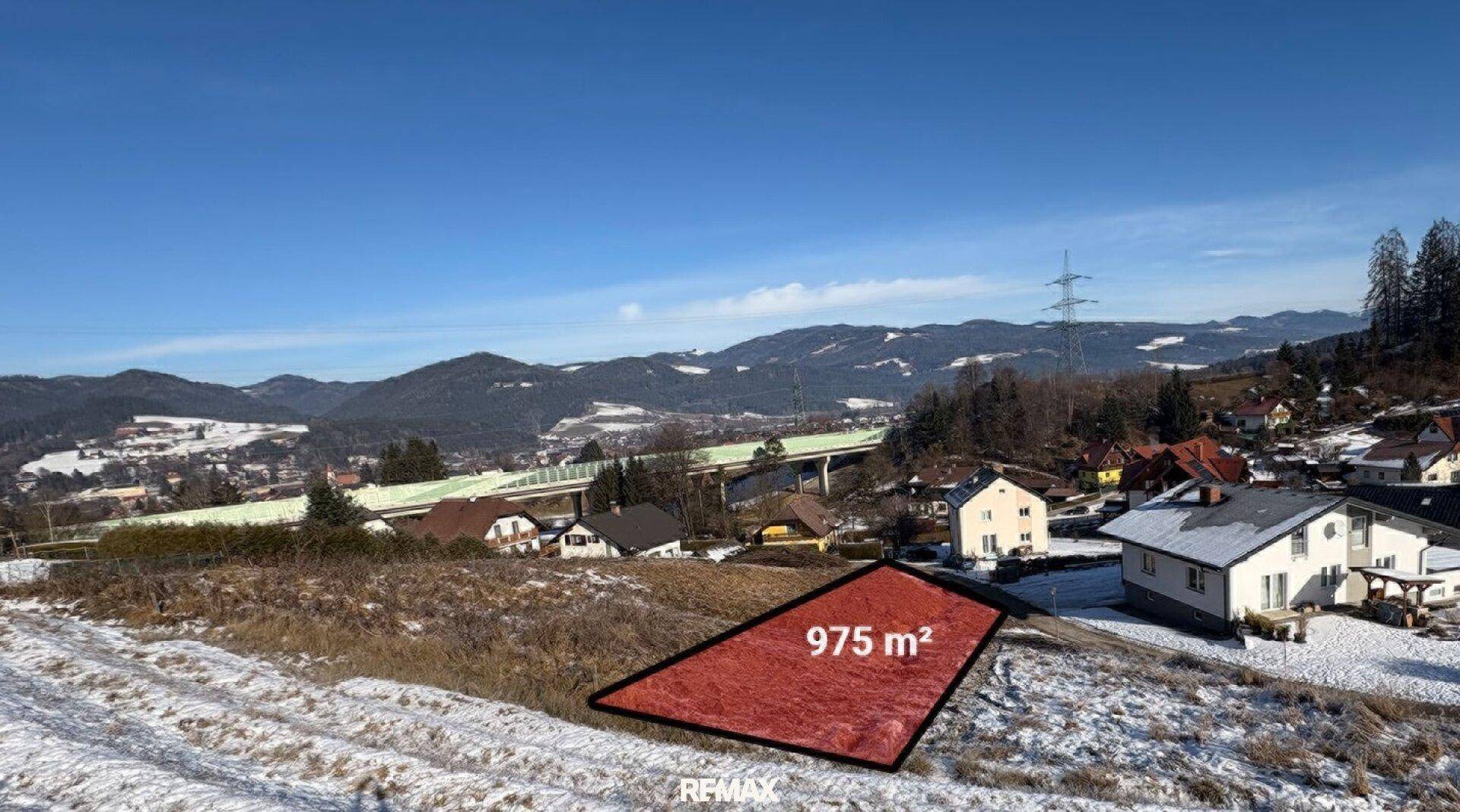 Winterliche Ansicht des Baugrundstücks von 975 m² mit schneebedeckten Hügeln und Häusern.