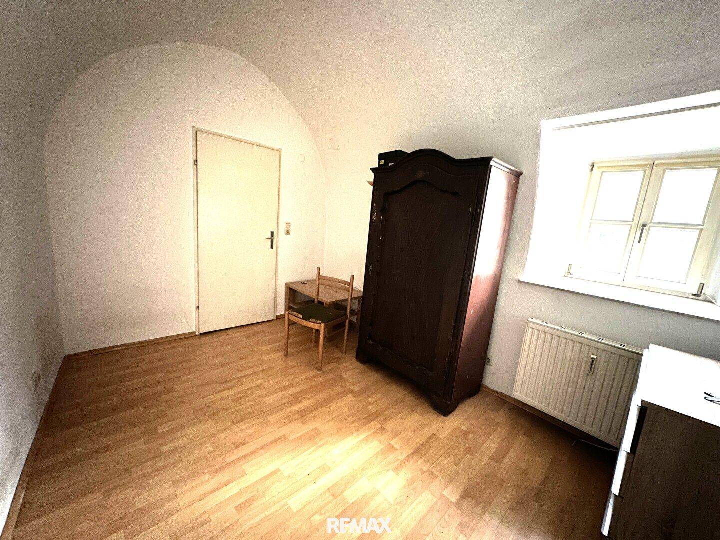 Helles Schlafzimmer mit Holzboden, gewölbter Decke und einem Fenster, das viel Licht hereinlässt.