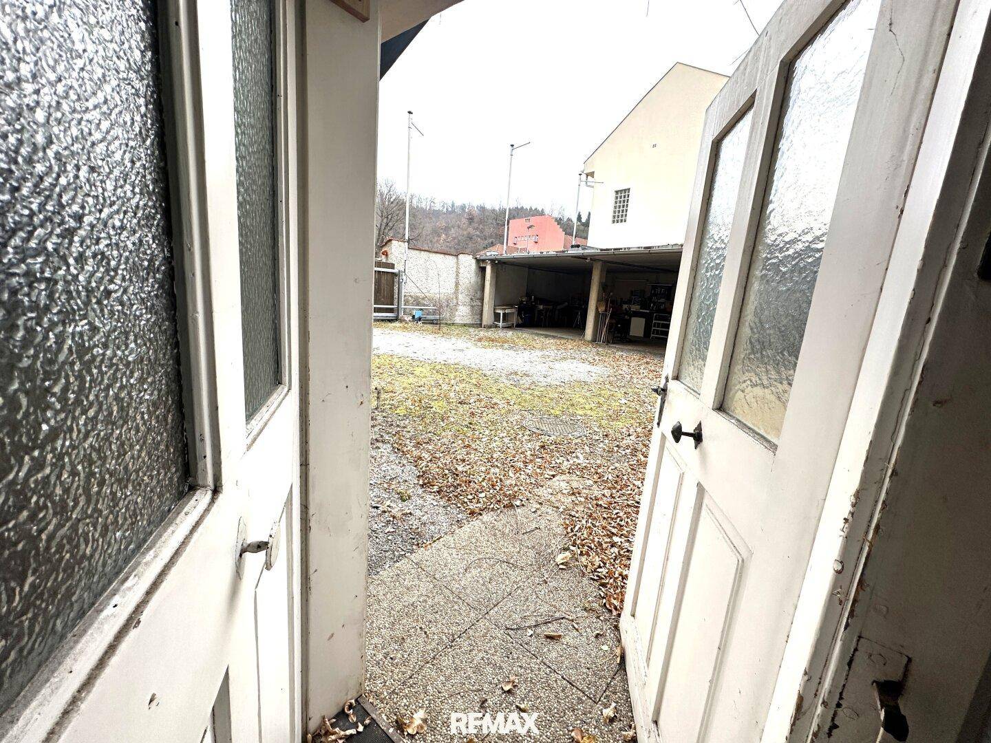 Hinterhof mit Rasenfläche und einer Garage im Hintergrund, zugänglich durch eine Doppeltür.