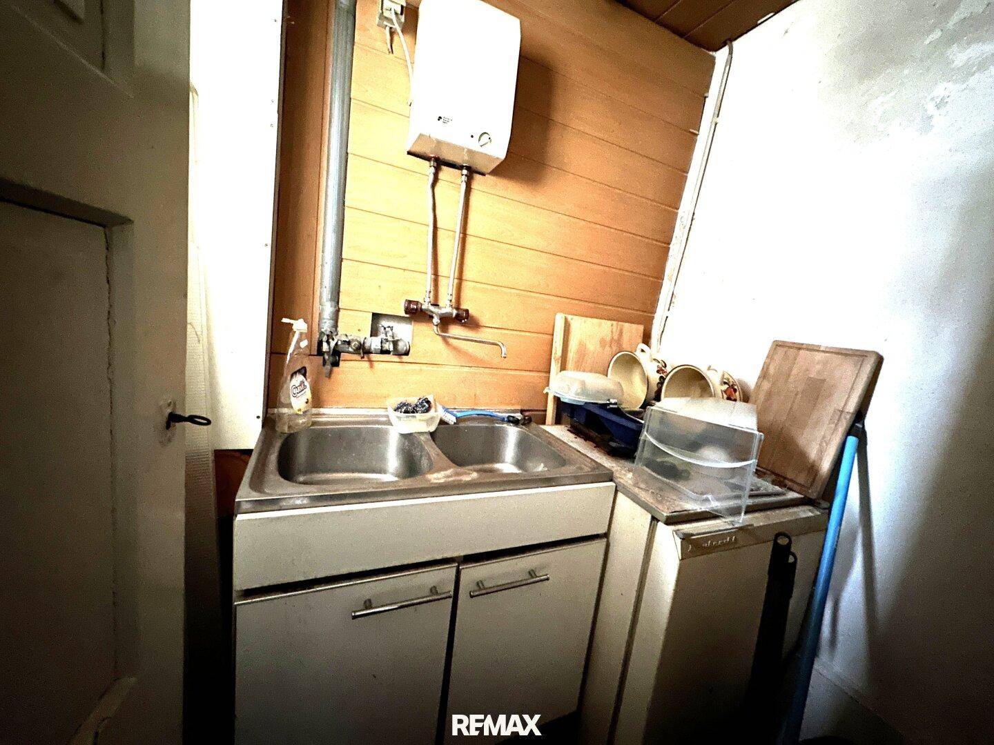 Kleiner Hauswirtschaftsraum mit Doppelwaschbecken, Warmwasserbereiter und Holzverkleidung.